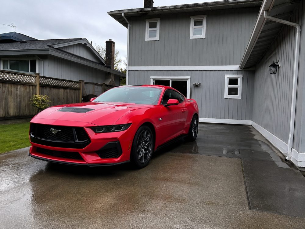 A red Ford Mustang on a wet driveway, freshly washed