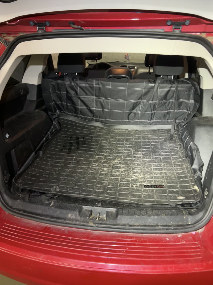 An SUV cargo area before cleaning, dirt across the boot liner